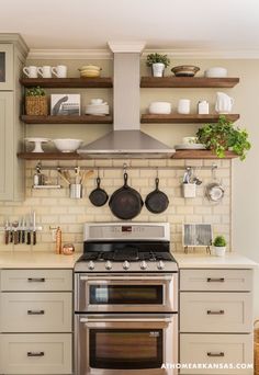 a stove top oven sitting inside of a kitchen next to wooden shelves filled with pots and pans