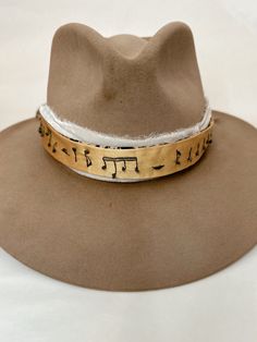 Hand embroidered hat band with musical notes embroidered along length. Band is a golden yellow color with dark gray embroidery and is reversible. Alternate side is a tan/brown basic fabric. Gold Wide Brim Fedora For Festivals, Gold Fedora Hat For Rodeo, Gold Fedora With Short Brim For Festivals, Gold Wide Brim Hat For Festivals, Gold Wide Brim Festival Hat, Gold Fedora Western Hat, Gold Brimmed Hat For Rodeo, Gold Flat Brim Hat For Rodeo, Gold Western Fedora Hat