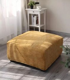 a yellow footstool sitting on top of a wooden floor next to a white table