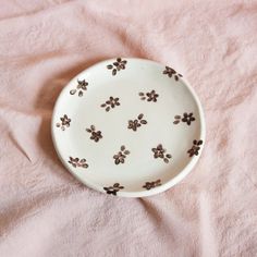 a white plate with brown flowers on it sitting on a pink cloth covered tablecloth