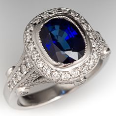 This glimmering ring is centered with one (1) bezel set cushion cut sapphire that is bordered by twenty-one (21) bead set round brilliant cut diamonds. The shoulder and side faces of the ring are set with sixty-eight (68) bead set round brilliant cut diamonds, and six (6) bezel set round brilliant cut diamonds. The ring has milgrain edging.  It measures 12.9mm at the top, rises 7.1mm above the finger, and tapers to 2.5mm wide by 1.5mm thick at the base of the shank. There are a few very light swirls in the platinum at the base of the shank.  The ring is currently a size 4.25. Luxury Cushion Cut Sapphire Diamond Ring, Luxury Gia Certified Cushion Cut Sapphire Ring, Formal Sapphire Ring With Brilliant And Cushion Cut, Formal Sapphire Ring With Cushion Brilliant Cut, Formal Cushion Cut Sapphire Ring With Diamond, Formal Fine Jewelry Sapphire Cushion Cut Ring, Cushion Cut Sapphire Diamond Ring For Formal Occasions, Luxury Lab-created Sapphire Ring For Formal Occasions, Formal Sapphire Cushion Cut Diamond Ring