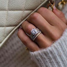 a woman's hand with two rings on it and a white purse in the background