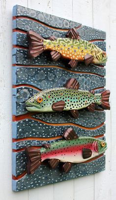 three fish are mounted to the side of a wall, each painted with different colors