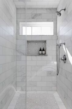 a walk in shower sitting next to a white tiled wall and floor covered in marble