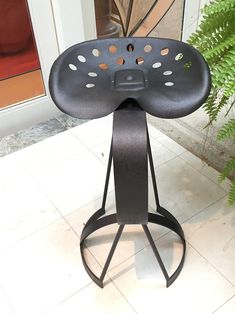 a black stool with holes on the back and seat is sitting next to a potted plant