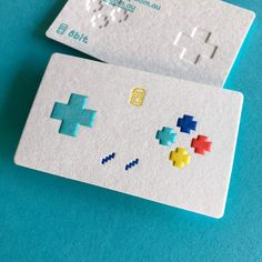 two white business cards with colored pixeles on them sitting next to each other in front of a blue background