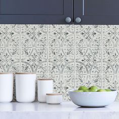 a bowl of green apples sitting on top of a counter next to two white cups