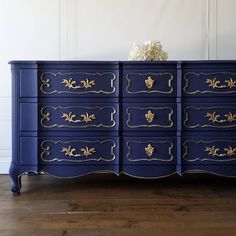 a blue and gold painted dresser with flowers on top