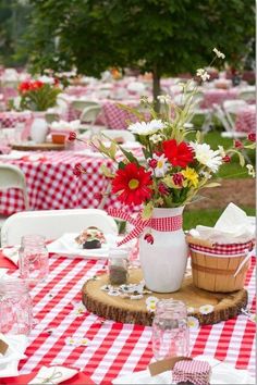 a red and white checkered table cloth with flowers in a vase on it,