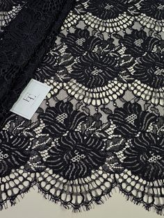 a black lace with white dots and fringes is on a tablecloth that has a tag attached to it