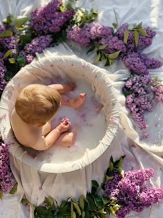 a baby in a bath surrounded by purple flowers