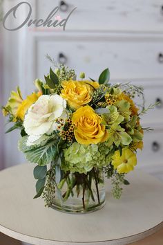 a vase filled with yellow and white flowers on top of a table next to a dresser