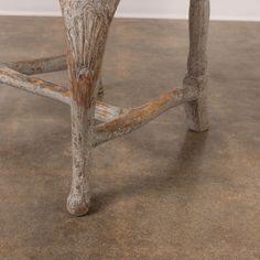 an old wooden bench with peeling paint on the legs and foot rests against a white wall