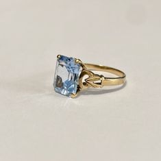 Beautiful 1940s era vintage 10k rosy yellow gold ring featuring a swiss blue topaz stone. The radiant blue topaz stone is radiant cut and secured by four prongs. The ring's shoulders are elegantly cinched with milgrain and repousse design details. Lovely piece of fine vintage jewelry, circa 1940! ERA - Circa 1940s / Retro METAL / MATERIAL - 10k gold, blue topaz MARKINGS / HISTORY - 10k SIZE / MEASUREMENTS - Size: 6 , Swiss Blue Topaz stone: approximately 10 x 8 mm, Weight: 2.15 grams, Shank: Tap Classic Topaz Birthstone Ring, Vintage Blue Gemstone Birthstone Ring, Vintage Blue Topaz Ring In 14k Gold, Vintage Blue Sapphire Ring Stamped 14k, Vintage Blue Topaz Ring With Prong Setting, Classic Light Blue Topaz Ring For Anniversary, Classic Light Blue Topaz Gemstone Ring, Classic Blue Topaz Ring, Vintage 14k Gold Topaz Ring With Center Stone