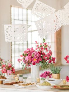 pink flowers are in vases on a table with plates and bowls full of food