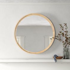 a white fireplace with a round mirror on the mantle and flowers in vases next to it