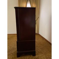 a tall wooden cabinet sitting on top of a carpeted floor next to a window