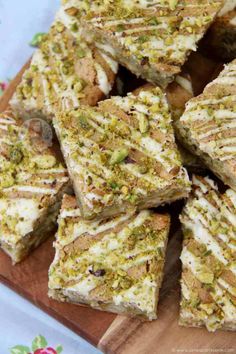 there are many pieces of cake on the cutting board with white frosting and pistachios