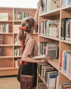 a girl standing in front of a bookshelf holding a book and looking at it