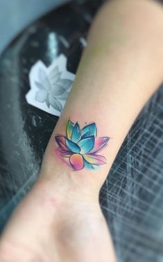 a lotus flower tattoo on the wrist is shown in this close up photo, it appears to be painted with watercolors