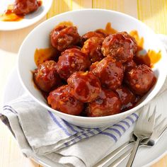 a white bowl filled with meatballs on top of a table next to silverware