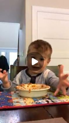 a little boy sitting at a table with a bowl of food in front of him