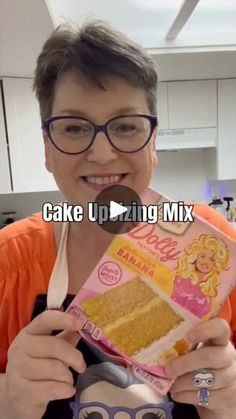 a woman holding up a box of cake next to an orange shirt and black glasses