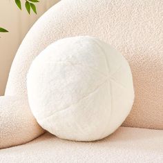 a large white pillow sitting on top of a couch next to a plant in a living room