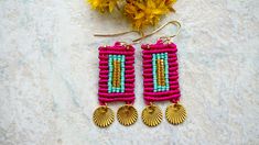 a pair of pink and blue beaded earrings next to yellow flowers on a white surface