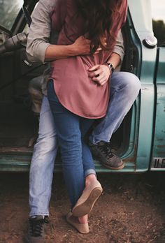 two people sitting on the back of a blue truck with their arms around each other