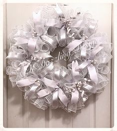 a white wreath with silver ribbon and pearls on the front door for someone's wedding