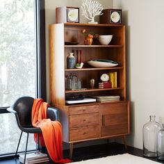 a room with a chair, table and bookshelf next to a large window