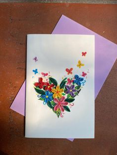 a greeting card with colorful flowers and butterflies in the shape of a heart on white paper