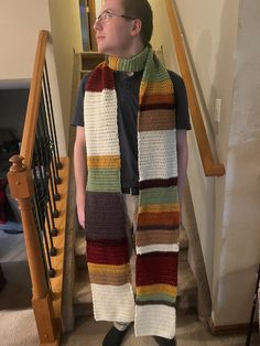 a man standing on the stairs wearing a multicolored striped scarf and black t - shirt