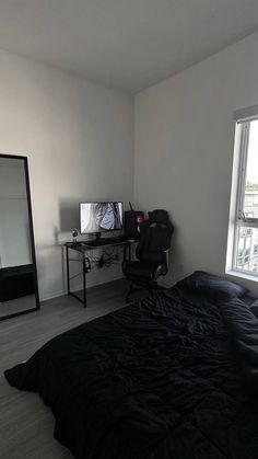 a bedroom with a bed, desk and tv in it's corner next to a large window