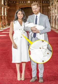 a man and woman holding a baby in a white dress on a red carpeted hall