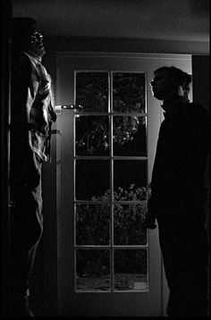 black and white photograph of two people standing in front of an open door at night