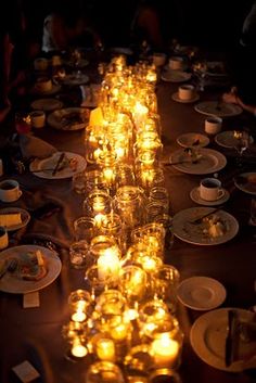 a long table with many plates and cups on it that have candles in the middle