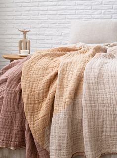 a bed covered in blankets and pillows next to a white brick wall