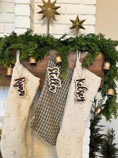 christmas stockings hanging from a mantel decorated with greenery