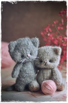 two gray teddy bears sitting next to each other on a table with pink flowers in the background