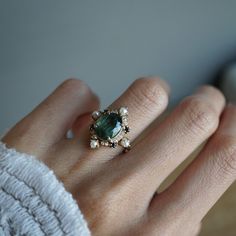 a woman's hand wearing a ring with an emerald and pearls on the side