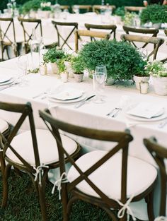 a long table with white linens and wooden chairs is set for an outdoor dinner