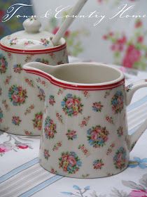 two white and red flowered teapots sitting on top of a floral table cloth