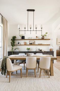 the dining room table is surrounded by white chairs and wooden shelves with plants on them