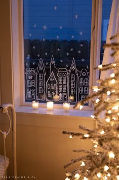 candles are lit in front of a window decorated with houses and snowflakes