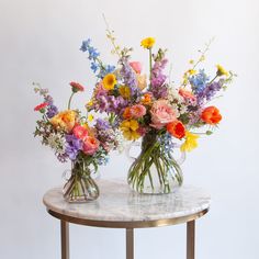 two vases filled with colorful flowers sitting on top of a marble topped side table