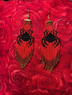 red and black beaded earrings sitting on top of a pink rose covered surface with roses