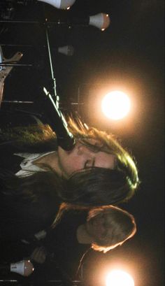 a woman with long hair standing in front of a microphone on stage at night time