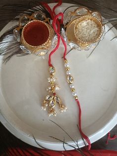 two gold and silver candles on a white plate with red string attached to the candle holders